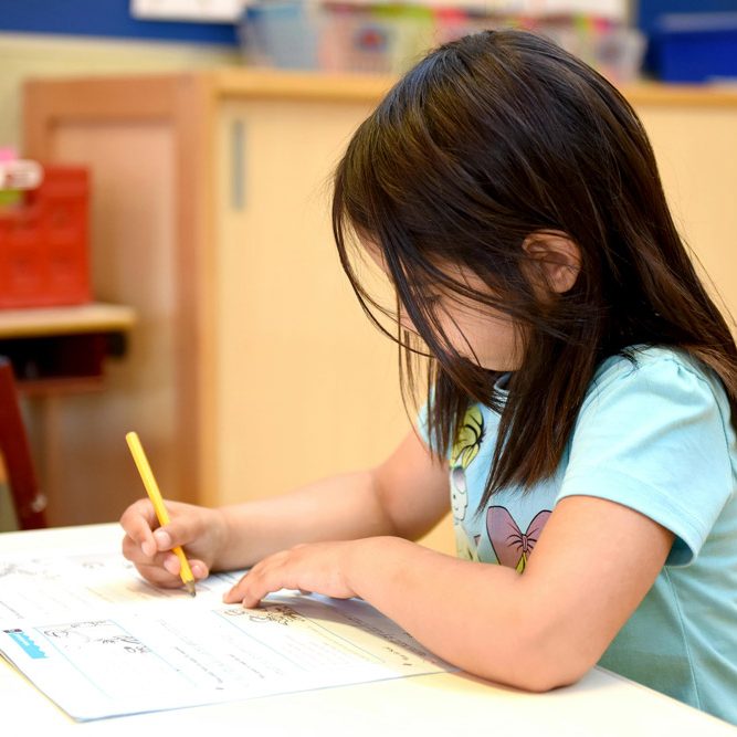 A Girl in Blue T-shirt Writing on a Book. Photo by Arthur Krijgsman.