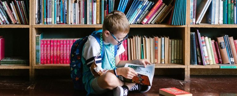 Child reading a book on the floor in front of a bookshelf. Image by RDNE Stock project.