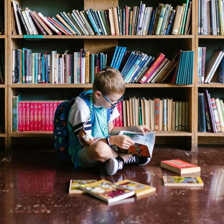 Child reading a book on the floor in front of a bookshelf. Image by RDNE Stock project.